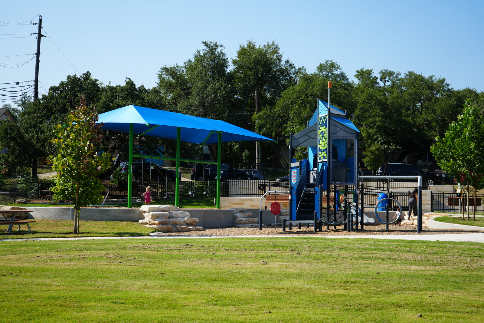 A shaded playground with swings and a climbing tower